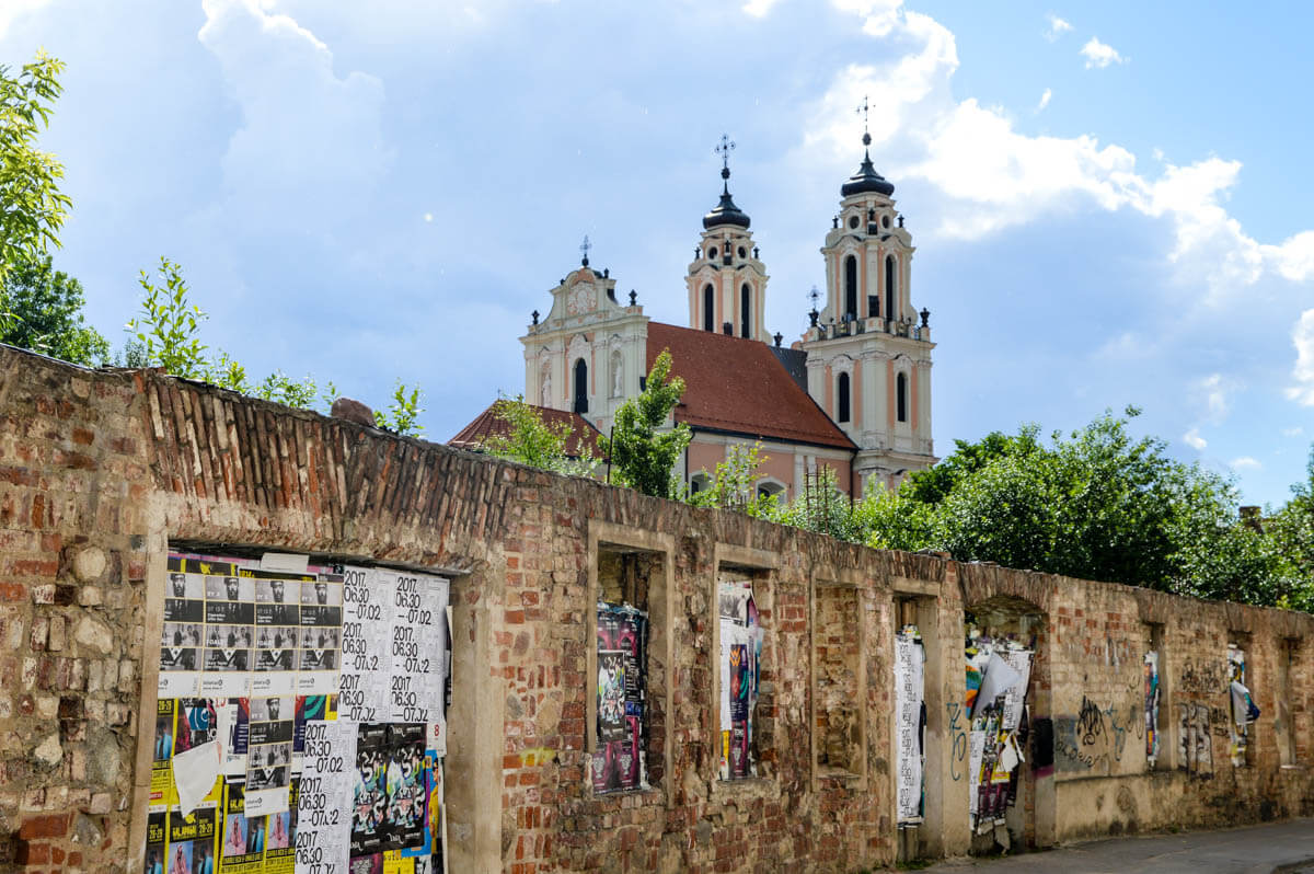 Vilnius Tipps für den Städtetrip: Heruntergekommene Mauer mit prunkvoller Kirche im Hintergrund